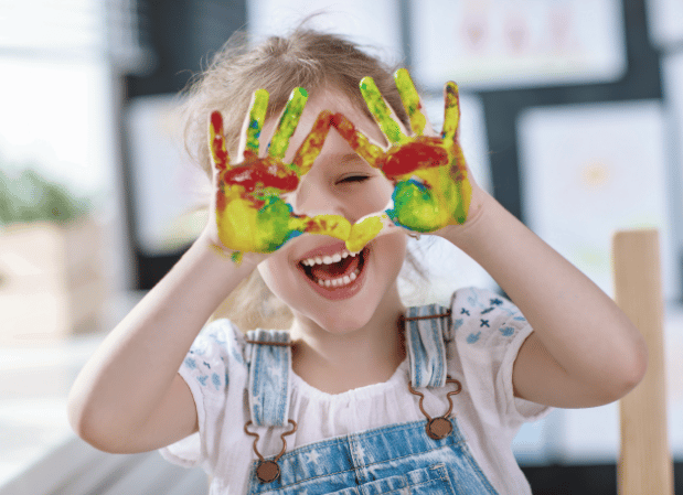a child laughing while holding up painted hands